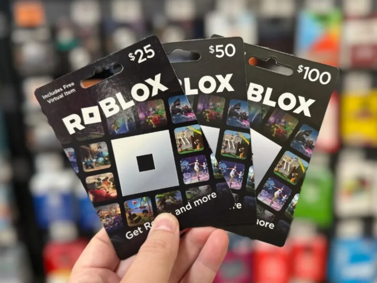 Hand holding Roblox gift card packaging with printed $25, $50, and $100 amounts
